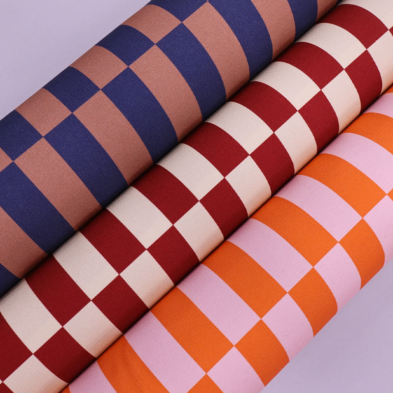 Three rolls of checkered fabric in blue, red, and orange on a light gray background