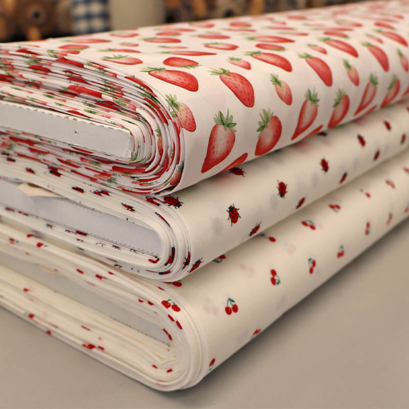 3 rolls of white cotton fabrics with a strawberry, ladybird and cherry print