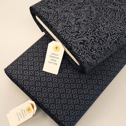 2 cotton fabric rolls featuring different grey designs on a black background