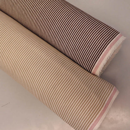 Two rolls of hickory striped denim fabric, one brown and white, one beige and white