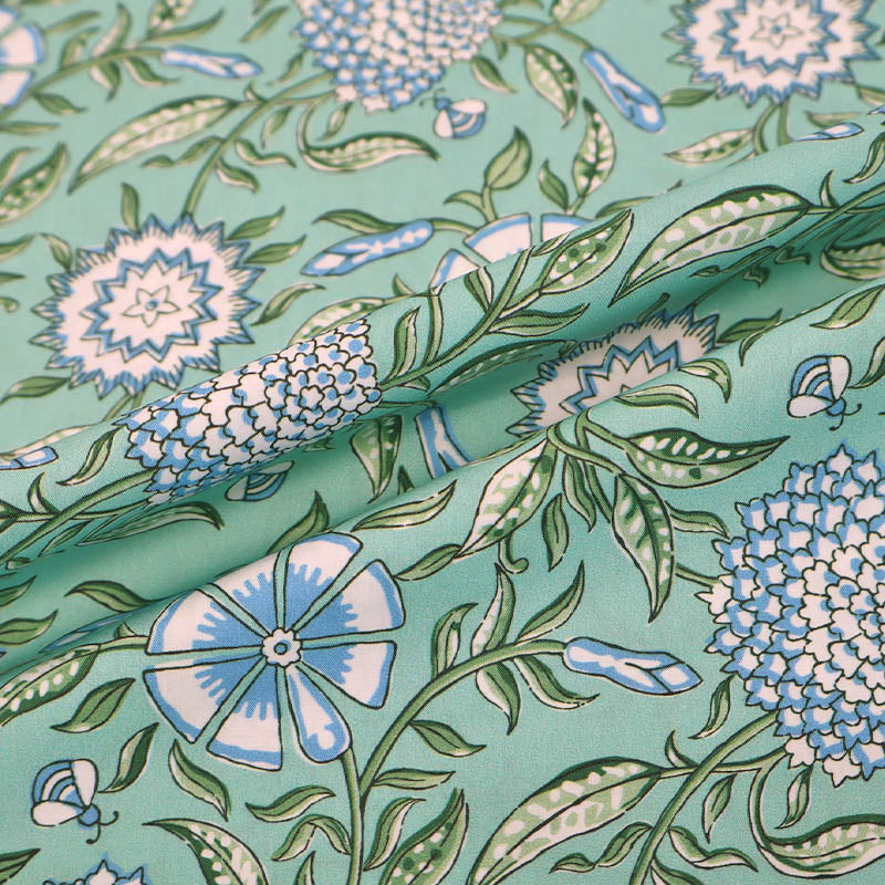  100% Cotton poplin fabric featuring a Digitally Printed pale blue and white floral and bee design with green leaves on a mint green background. 