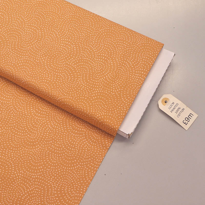 100% Cotton Orange Blender Fabric featuring a subtle print of white spots in a spiral on a soft orange background.