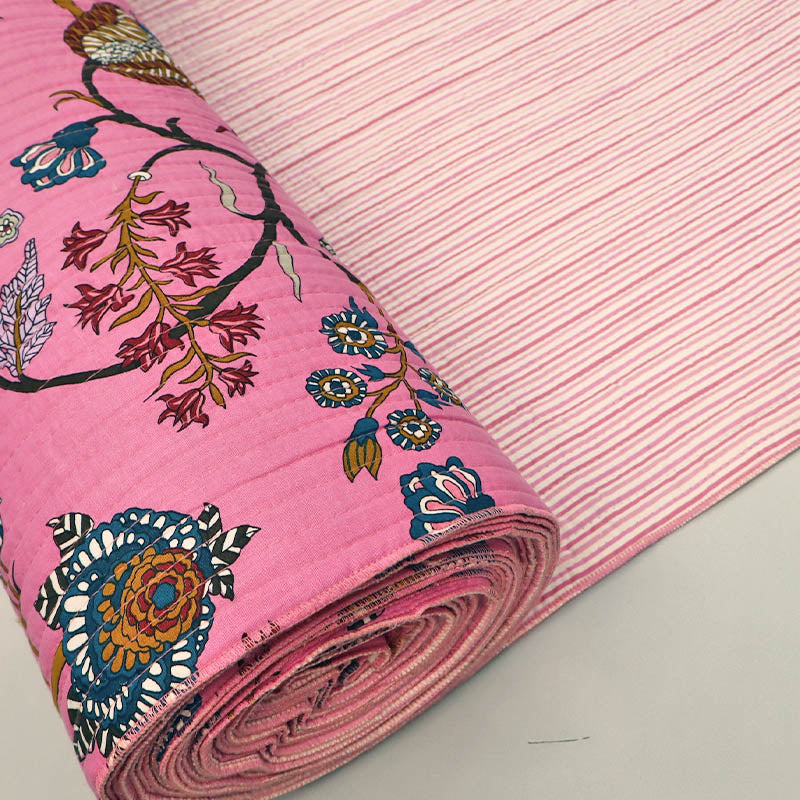Quilted 100% Indian cotton fabric with a bold floral design in pink, blue and brown on a sugar pink background on one side and a fine pale pink and white stripe on the reverse.