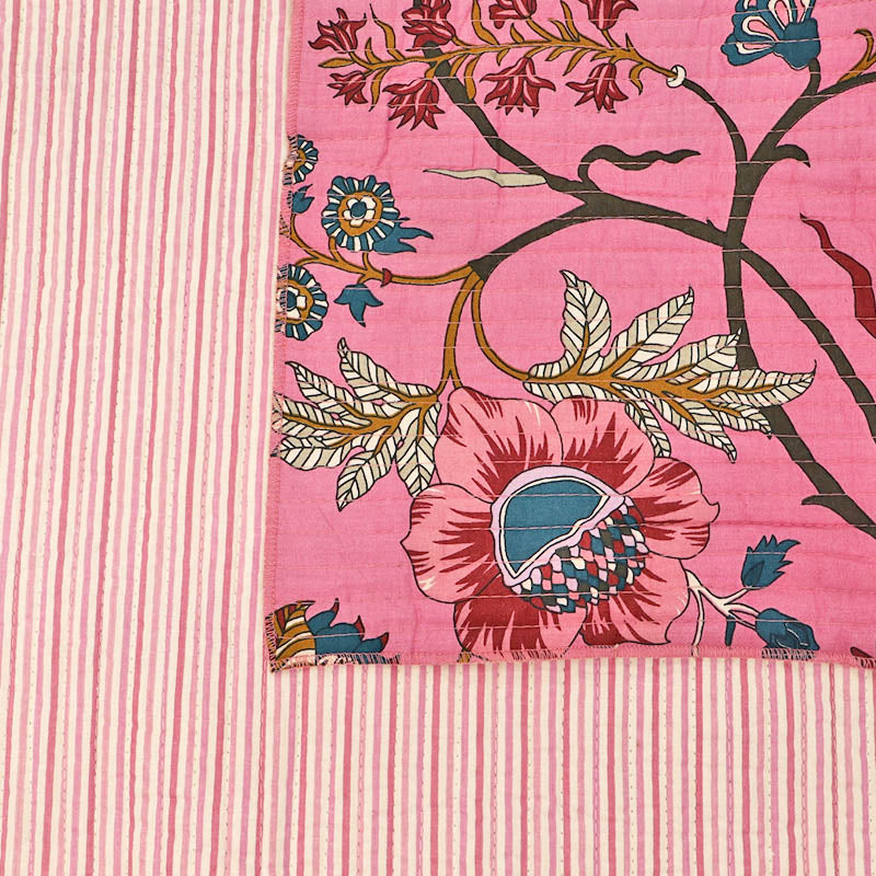Quilted 100% Indian cotton fabric with a bold floral design in pink, blue and brown on a sugar pink background on one side and a fine pale pink and white stripe on the reverse.