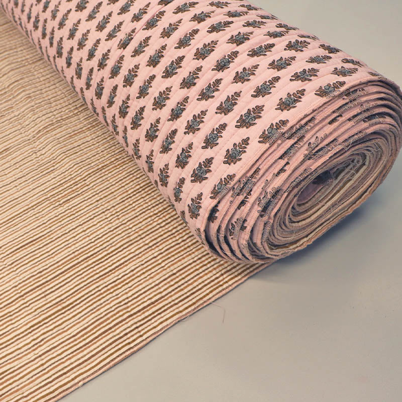 Quilted 100% Indian cotton fabric with a floral motif in brown and grey on a pale pink background on one side and a fine beige and cream stripe on the reverse.